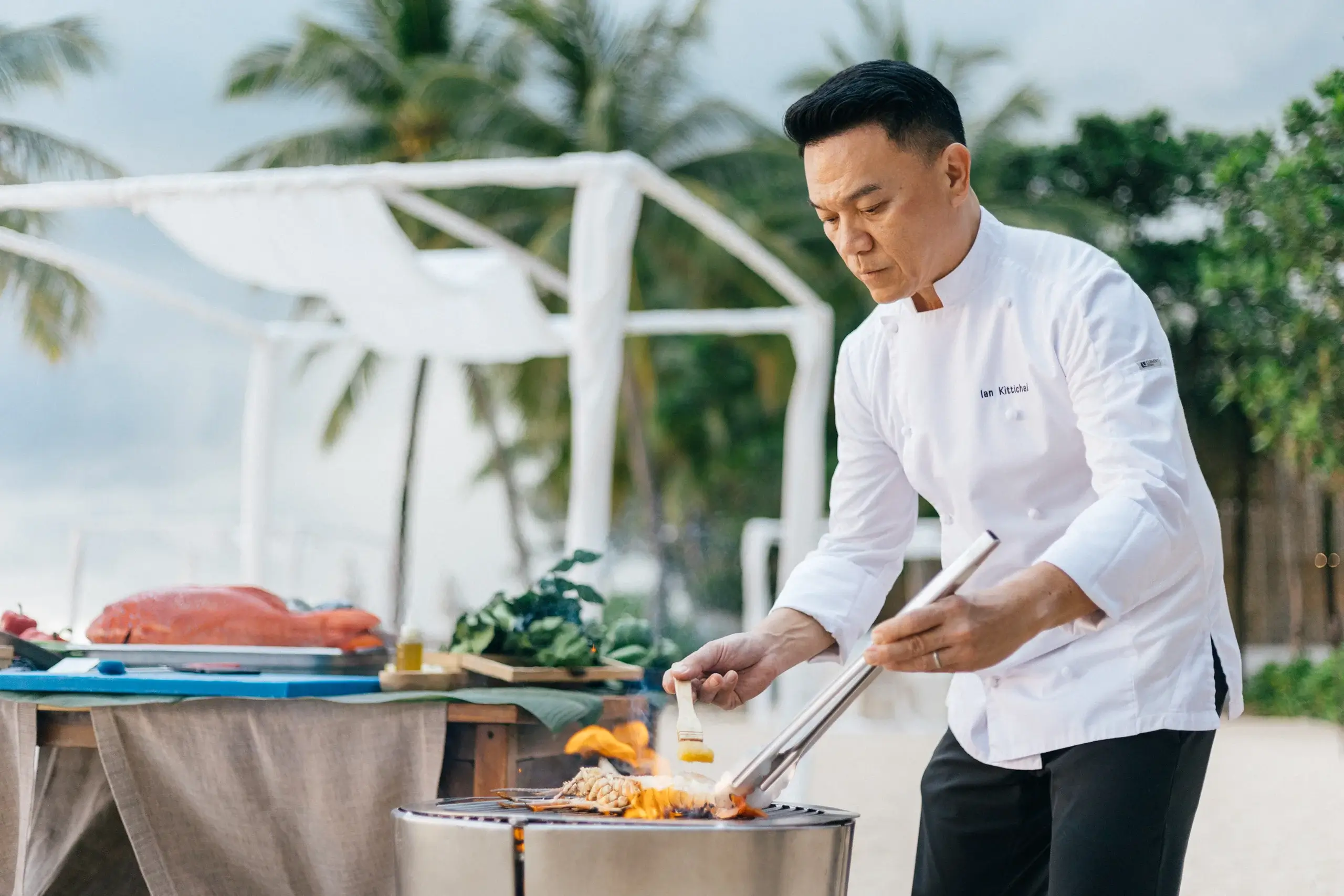 Ian cooking over a grill flame on a beach in bahamas