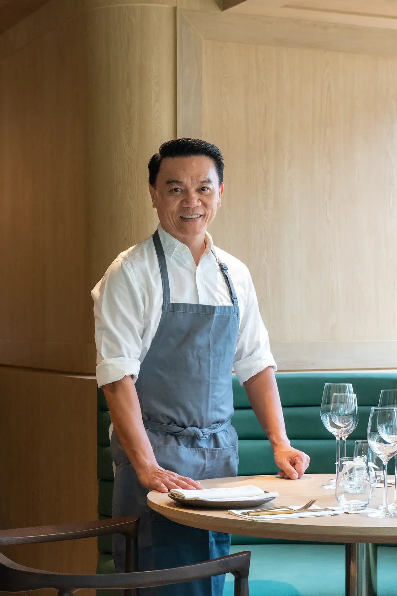 Ian standing over a table at his restaurant. the table is prepared with wine glasses