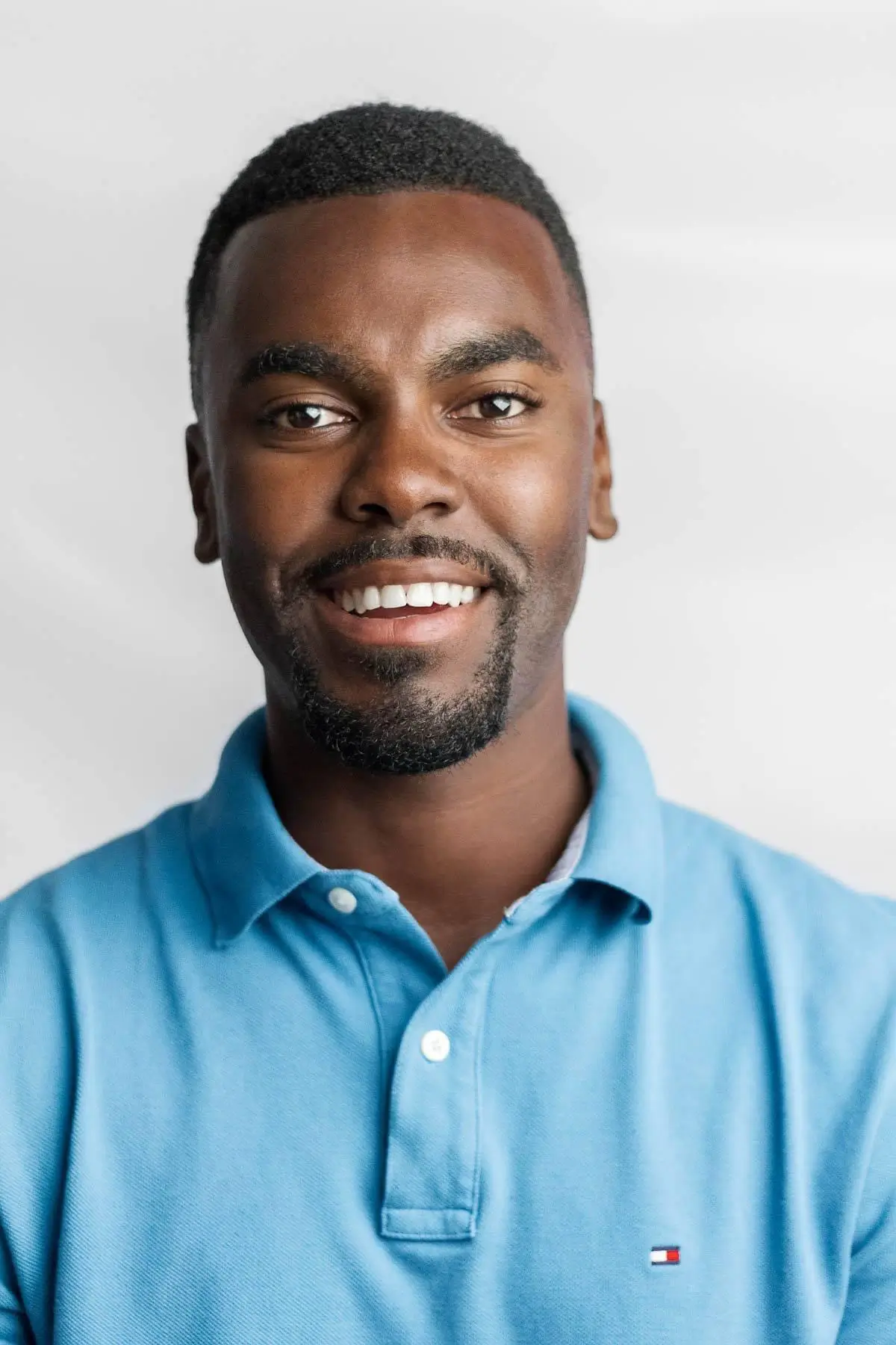 Close-up portrait of a smiling person wearing a light blue polo shirt against a light background.
